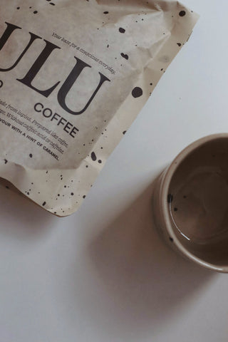 Stand up pouch of lupine coffee close-up with a lulu ceramics cup with black splashes on white background minimalistic set-up.