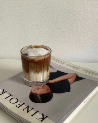 Iced Lulu Latte in einem hohen Glas auf einem Kinfolk-Buch – Lupinenkaffee über Eis mit Milch, im editorialen Flat-Lay-Stil.